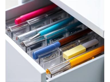 Clear acrylic drawer dividers configured in a drawer filled with neatly separated office supplies like pens, staplers, and sticky notes, illustrating organized compartments.